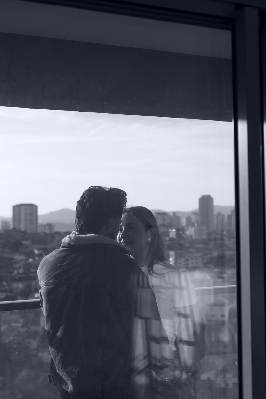 Os dois de costas na janela, a cidade lá embaixo